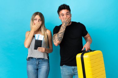 Genç beyaz çift mavi arka planda izole bir şekilde seyahat edecek. Ağızlarını uygunsuz bir şey söyledikleri için elleriyle kapatacaklar.