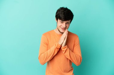 Mavi arka planda izole edilmiş genç bir Rus avuç içlerini bir arada tutuyor. İnsan bir şey ister.