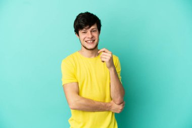 Genç Rus adam mavi arka planda yalnız gülüyor.