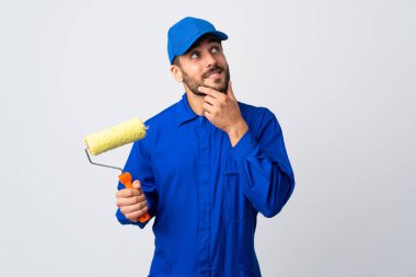 Boyacı beyaz arka planda izole edilmiş bir boya silindiri tutuyor. Yukarı bakarken bir fikir düşünüyor.