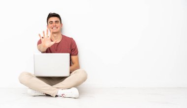 Flor 'da dizüstü bilgisayarıyla oturan genç adam parmaklarıyla beşi sayıyor.