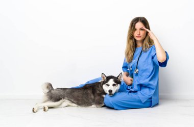 Sibirya Husky köpeği olan veteriner doktor yerde mutsuz ve hayal kırıklığına uğramış bir şekilde oturuyor. Olumsuz yüz ifadesi