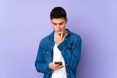 Kafkasyalı yakışıklı bir genç. Mor arka planda izole edilmiş. Düşünüyor ve mesaj gönderiyor.