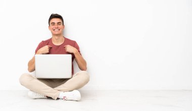 Flor 'da dizüstü bilgisayarıyla oturan genç bir adam. Sürpriz bir yüz ifadesi var.
