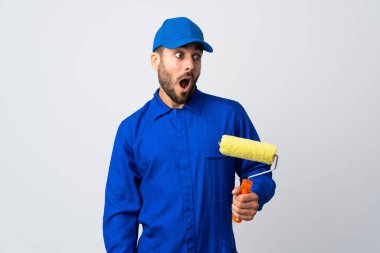 Beyaz arka planda izole edilmiş bir boya silindiri tutan ressam yan tarafa bakarken sürpriz jest yapıyor.