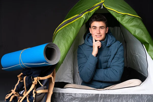 Teenager caucasian man inside a camping green tent isolated on black background Looking front