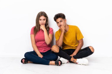 Genç bir çift, beyaz arka planda izole bir şekilde yerde oturuyor.