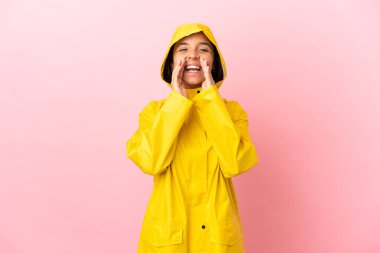 Yağmura dayanıklı bir ceket giyen genç Latin bir kadın izole edilmiş arka planda bağırıyor ve bir şey duyuruyor.