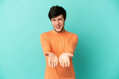 Genç Rus bir adam mavi arka planda izole edilmiş. Kopyalama alanı hayali bir ilan vermek için avucunun içinde duruyor.
