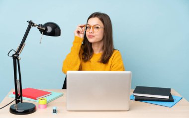 Evinde okuyan öğrenci kız mavi arka planda gözlüklü ve mutlu.