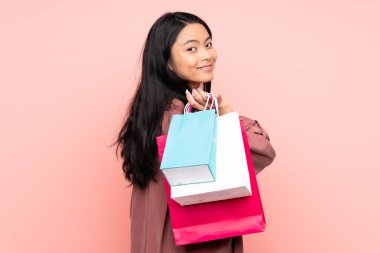 Genç Çinli kız pembe arka planda izole edilmiş. Elinde poşetler ve gülümsüyor.