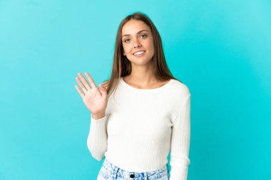 Soyutlanmış mavi arka planda genç bir kadın. Mutlu bir ifadeyle selamlıyor.