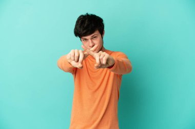Genç Rus adam mavi arka planda izole edilmiş bir şekilde bir eylemi durdurmak için eliyle jest yapıyor.
