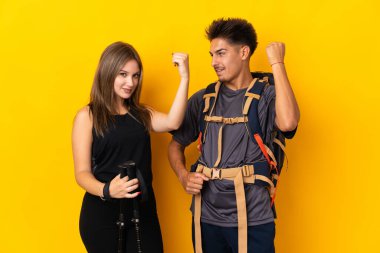 Sarı arka planda büyük bir sırt çantası olan genç dağcı çift galibiyetlerini kutluyorlar.