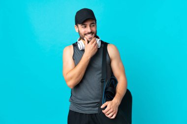 Spor çantalı genç adam mavi arka planda izole edilmiş, yana bakıyor ve gülümsüyor.