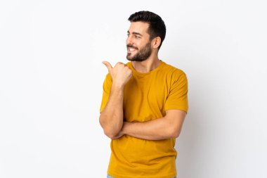 Beyaz arka planda sakallı yakışıklı genç bir adam bir ürün sunmak için kenarı işaret ediyor.