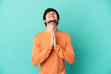 Mavi arka planda izole edilmiş genç bir Rus avuç içlerini bir arada tutuyor. İnsan bir şey ister.