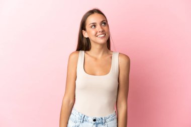 Soyutlanmış pembe arka planı olan genç bir kadın yukarı bakarken bir fikir düşünüyor.
