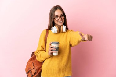 Tecrit edilmiş pembe arka planda genç bir bayan baş parmak hareketi yapıyor.