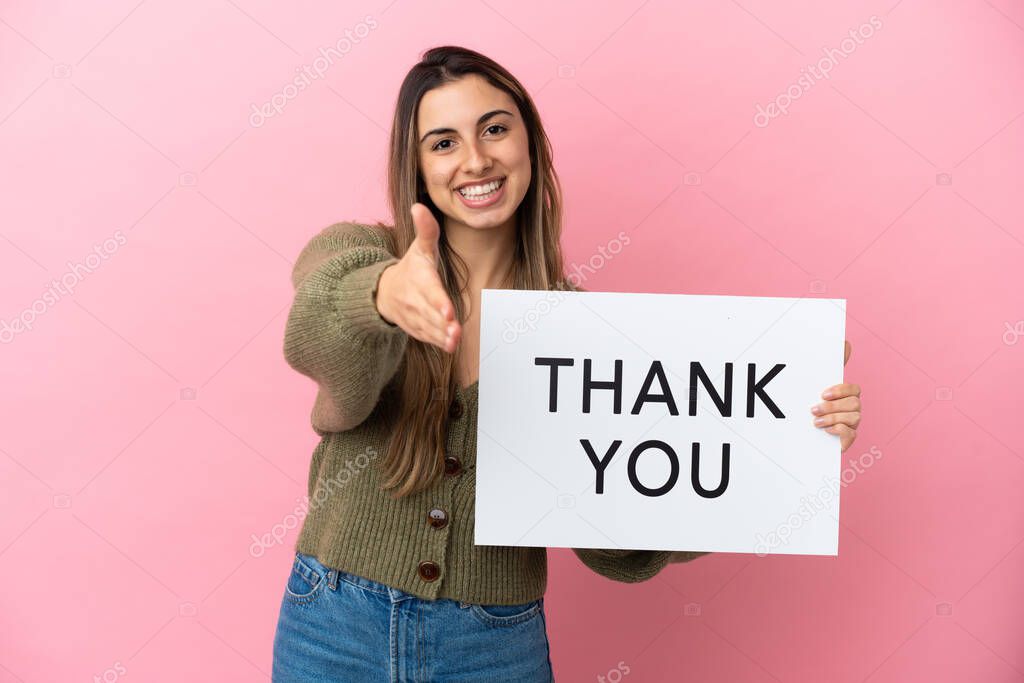 Young caucasian woman isolated on pink background holding a placard with text THANK YOU making a deal