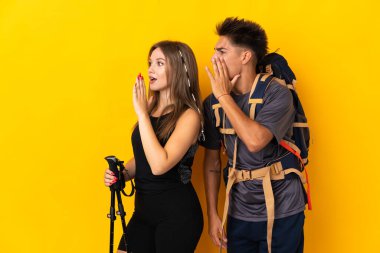 Sarı arka planda izole edilmiş büyük sırt çantalı genç dağcı çift ağızları sonuna kadar açık bağırıyor.