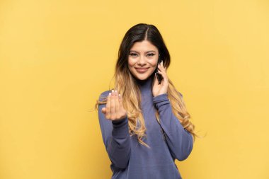 Sarı arka planda izole edilmiş cep telefonu kullanan genç bir Rus kızı bizimle gelmesi için davet ediyor. Gelmene sevindim.