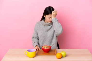 Genç Çinli kız baş ağrısı olan bir masada kahvaltı yapıyor.