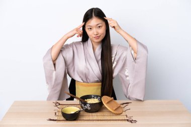 Genç Çinli kız kimono giyiyor, erişte yiyor şüpheleri var ve düşünüyor.