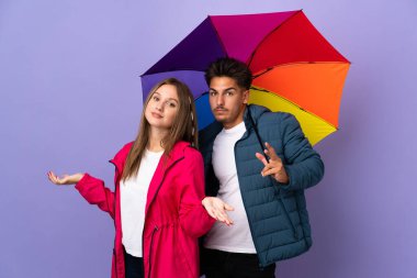 Mavi arka planda şemsiye tutan çift ellerini ve omuzlarını kaldırırken şüpheye düşüyor.