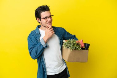 Rus adam, sarı arka planda izole edilmiş şeylerle dolu bir kutuyu kaldırırken harekete geçiyor ve yan tarafa bakıyor ve gülümsüyor.