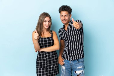 Kafkasyalı genç bir çift mavi arka planda izole edilmiş. İyi bir şey olduğu için iyi bir jest yapıyorlar.