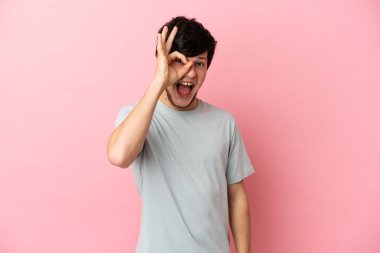 Pembe arka planda izole edilmiş genç Rus adam parmaklarıyla tamam işareti gösteriyor.