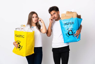 Plastik ve kağıt dolu bir çanta taşıyan genç bir çift beyaz arka planda izole edilmiş bir fikir düşünüyorlar.