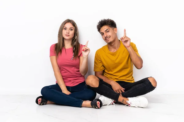 白い背景に隔離された床の上に座っている若いカップルは 最高の兆候で指を見せて持ち上げる — ストック写真