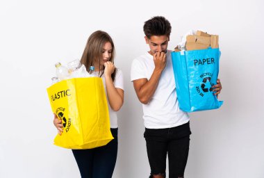 Plastik ve kağıt dolu bir çanta taşıyan genç çift beyaz arka planda kuşkuları olmadan izole edilmiş.