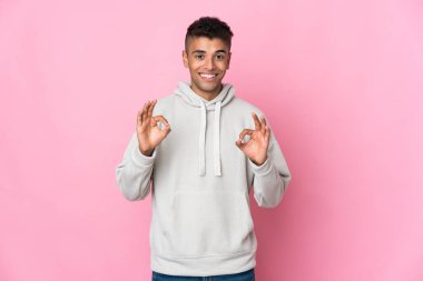 Pembe arka planda izole edilmiş genç Brezilyalı iki eliyle tamam işareti gösteriyor.