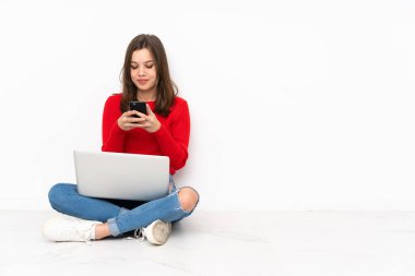 Bilgisayarla çalışan tenaager kız beyaz arkaplanda izole edilmiş olarak cep telefonuyla bir mesaj gönderiyor