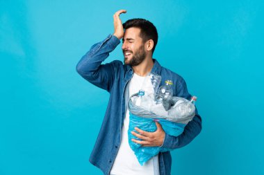 Mavi arka planda izole edilmiş plastik şişelerle dolu bir çanta taşıyan genç beyaz adam bir şeyin farkına vardı ve çözüme niyetlendi.