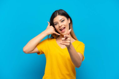 Genç Rus kız, mavi arka planda izole edilmiş telefon hareketi yapıyor ve ön tarafı işaret ediyor.