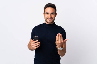 Beyaz arka planda izole edilmiş cep telefonu kullanan genç beyaz bir adam bizimle gelmesi için davet ediyor. Gelmene sevindim.
