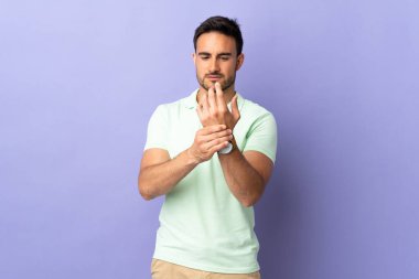 Mor arka planda izole edilmiş genç yakışıklı adam ellerindeki acıdan muzdarip.