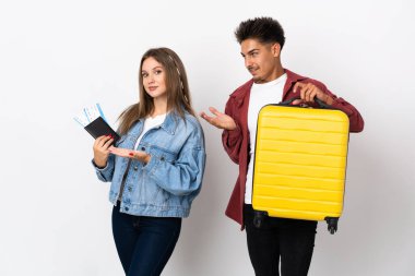 Gezgin çift mavi arka planda izole edilmiş bir bavul tutuyor. Davet etmek için ellerini yana uzatıyor.