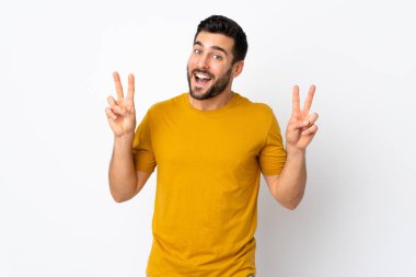 Beyaz arka planda sakallı yakışıklı genç adam iki eliyle zafer işareti gösteriyor.