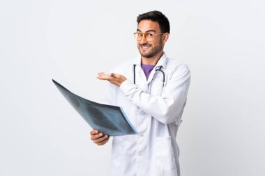 Genç bir doktor beyaz arka planda izole edilmiş bir radyografi tutuyor. Gelmesi için ellerini yana uzatıyor.