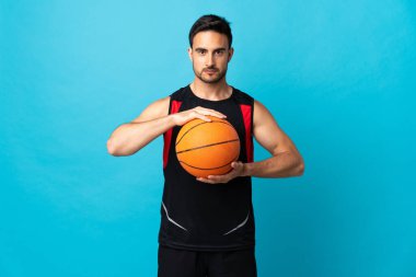 Genç yakışıklı adam mavi arka planda izole edilmiş basketbol oynuyor.