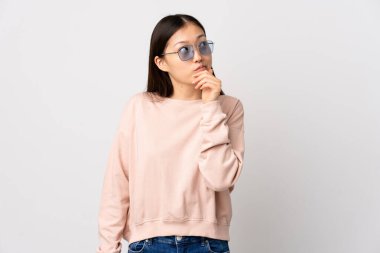 Soyutlanmış beyaz arka planı olan genç bir Çinli kızın şüpheleri ve kafa karıştırıcı bir yüz ifadesi var.