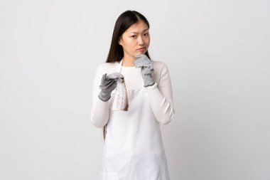 Çinli balıkçı önlük takıyor ve çiğ balığı izole edilmiş beyaz arka planda tutuyor. Şüpheleri ve düşünceleri var.