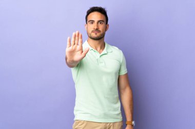 Mor arka planda izole edilmiş genç yakışıklı adam dur hareketi yapıyor.