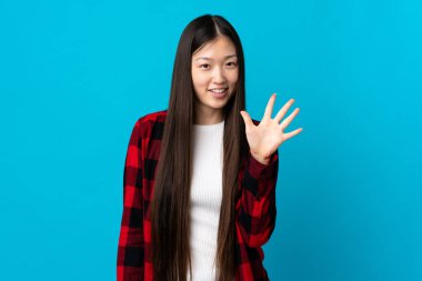 İzole edilmiş mavi arka plan üzerinde genç Çinli kız parmaklarıyla beşi sayıyor.