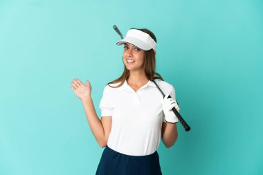 İzole edilmiş mavi arka planda golf oynayan kadın, davet edilmek için ellerini yana uzatıyor.